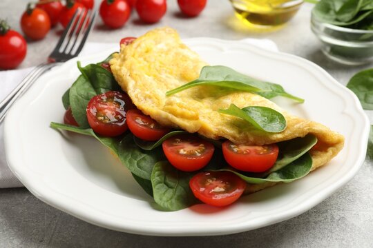 Tasty omelette with spinach and tomatoes served on light grey table, closeup