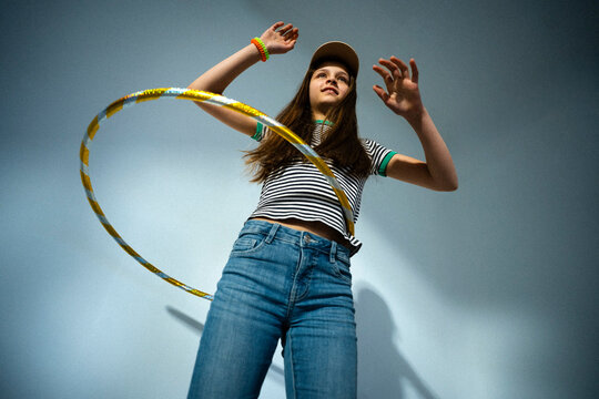 Low angle view of girl spinning hula hoop near blue wall