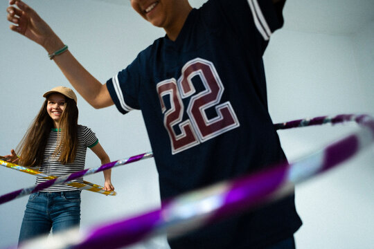 Happy siblings spending leisure time spinning hula hoops against colored background