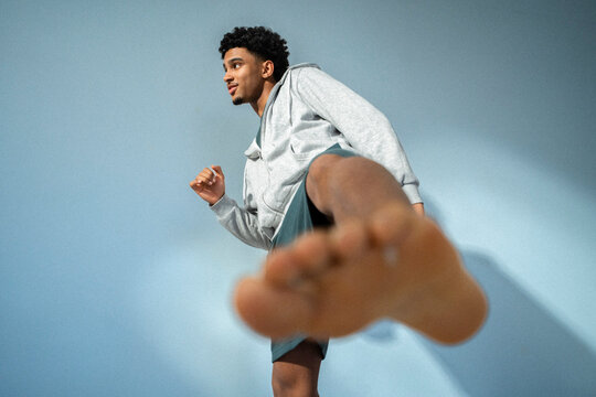 Young man practicing martial arts move against colored background