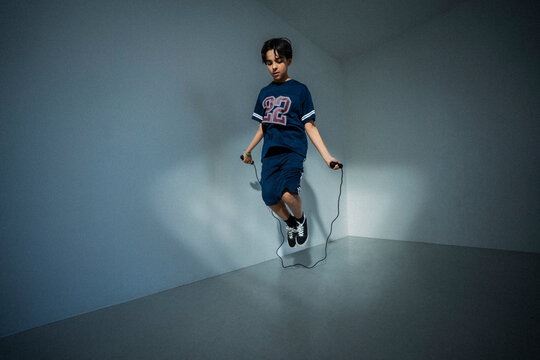 Full length of boy practicing jumping rope skills amidst blue walls
