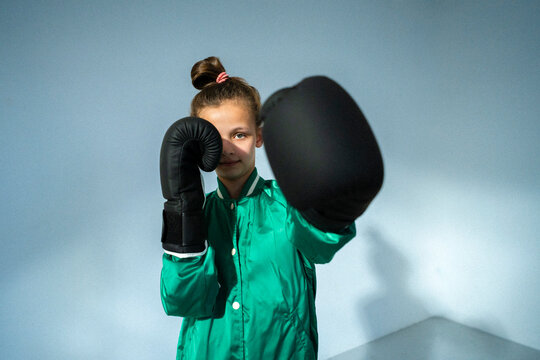Portrait of girl wearing varsity jacket posing with black boxing glove against wall