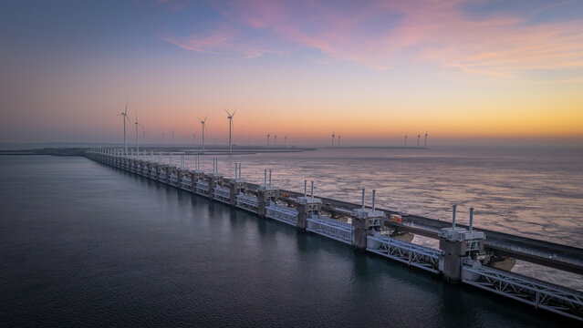 Aerial view of the Oosterscheldekering storm surge barrier and offshore wind turbines under a vibrant sunset sky in Vrouwenpolder, Zeeland, Netherlands.