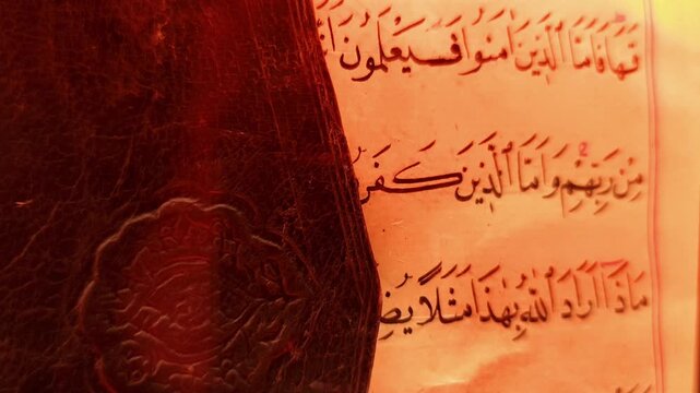 Static close-up shot showing the weathered edge and spine of an ancient Quran manuscript beside a page of elegant Arabic calligraphy