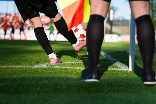 Low angle shot of a soccer player kicking a ball from a corner with a referee's flag and legs in the foreground.