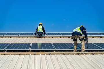 Fototapeta premium A professional technician in safety gear standing on a rooftop, preparing electrical wiring for a solar panel installation under a clear blue sky.