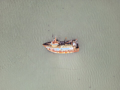 Aerial view of a rusty abandoned fishing boat floating in calm murky water with a weathered hull and deck equipment.
