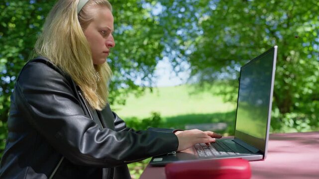 Side View of Concentrated Young Woman Working on Laptop in Park: Concept of Outdoor Office, Digital Nomadism, and Remote Freelancing