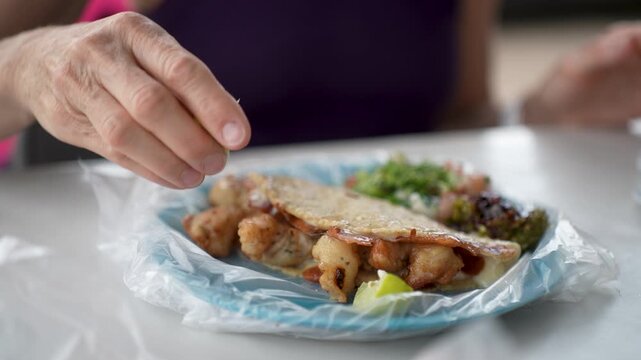 Mature woman eats shrimp tacos from a taco stand in Baja California Mexico and adds lime to enhance flavor during her meal