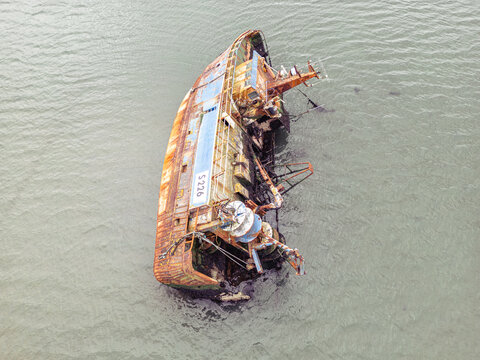 Aerial view of a rusted and partially submerged shipwreck with the identification S 226 on its side in murky coastal waters.