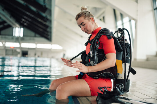 Woman diver preparing scuba gear for training in an indoor swimming pool, practicing diving skills and safety