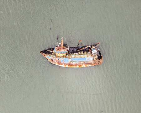 Aerial view of a rusty blue and orange fishing trawler floating on calm murky water.