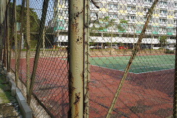 View of an outdoor sports court through a rusty chain-link fence © Wawan