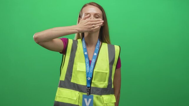 Woman volunteer wearing a yellow reflective safety vest and volunteer lanyard places right hand flat across chest while smiling at camera in studio; community service duty.