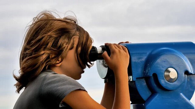 young child looking through blue tourist telescope against cloudy sky