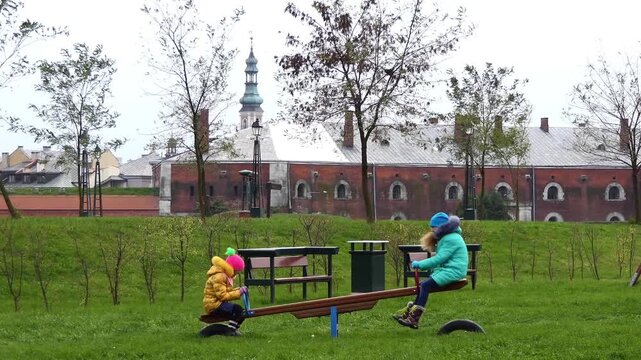 Two girls swinging on a swing in the park in autumn near the old town of Zamosc, Poland.