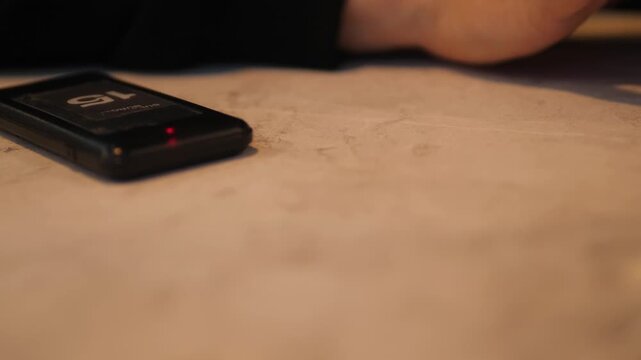 Wireless guest paging system pager flashing red light on a restaurant table. Customer waiting for food order readiness in a modern cafe.