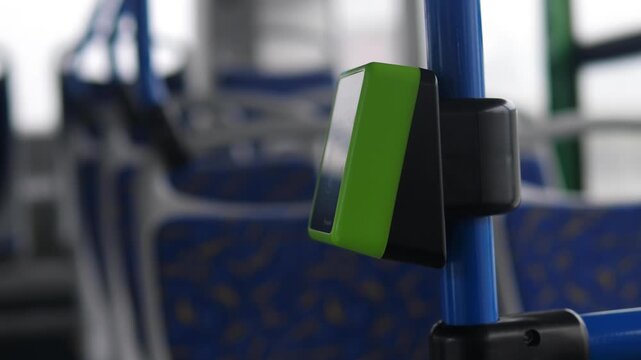 Green contactless validator for fare payment installed on a handrail in an empty modern bus. Automated payment system technology in urban public transport.