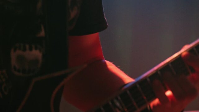 The musician's hand plays on neck of the guitar. The blue lighting of stage creates a gloomy atmosphere of a rock concert. Soft focus and dynamic perspective of live performance and musical energy