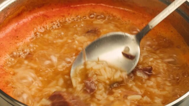 kharcho soup boiling and cooking close up, hot pot with greens rice and spoon spinning in a circle, georrgian restaurant, tomato soup macro. 