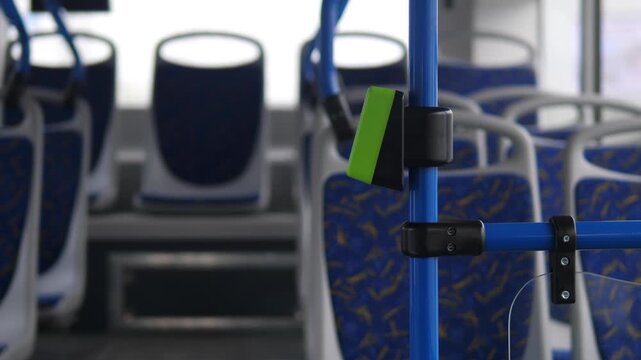 Interior of an empty modern bus with blue seats and a green validator on the handrail. Urban public transport cabin without passengers during daytime.
