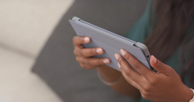 Adult African woman holding tablet folio case thumb tapping causing grip shifts on couch in teal