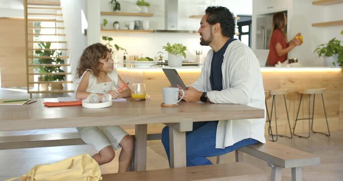 African American father and daughter leaning, showing tablet, helping child doing homework at table