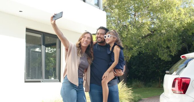 Family posing at driveway while mother raising phone for selfie daughter adjusting sunglasses