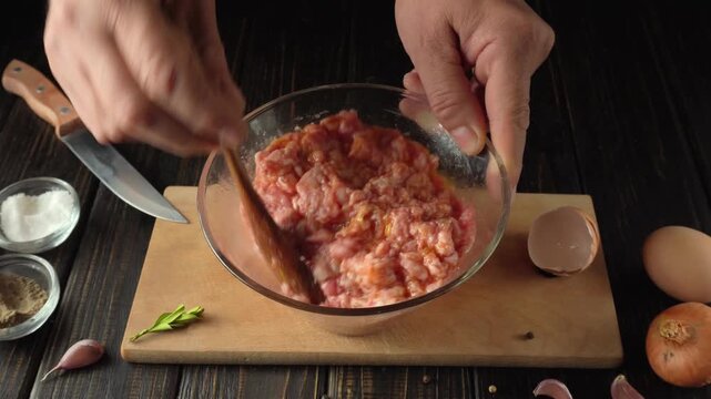 Hands mixing raw ground meat with spices and egg in a glass bowl on a wooden cutting board with garlic and onion in the background