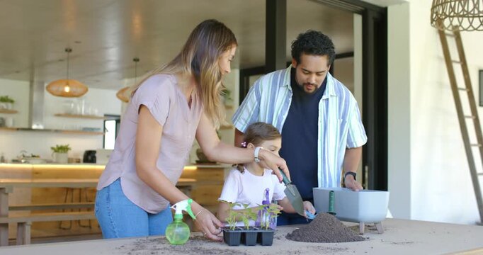 Family with preteen daughter placing seedling tray, planting at covered patio table mother guiding