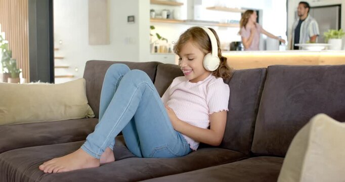 Diverse family girl wearing headset tapping phone sofa cam pulling back parents talking, copy space