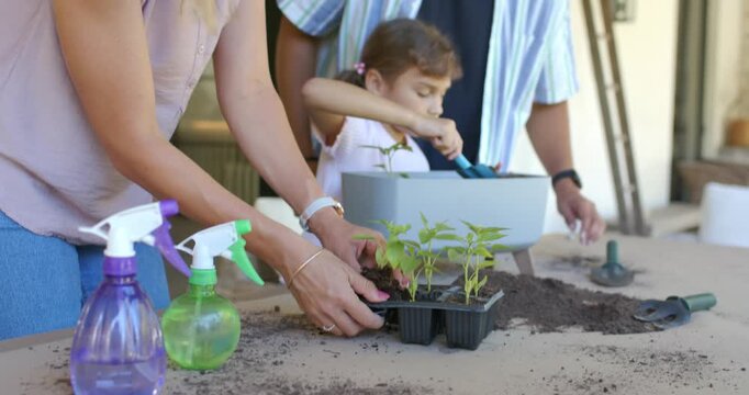 Parents and child planting from seed trays scooping soil with blue trowel filling planter on porch