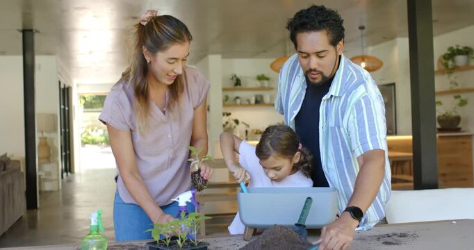 Diverse family guiding child at table, scooping soil with trowel into planter, potting seedlings