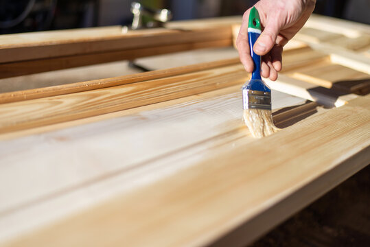 Applying protective varnish on wooden door with paint brush