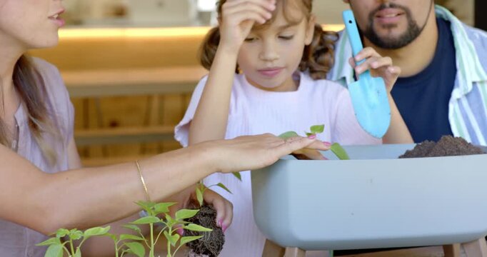 Family parents girl planting into grey planter at table with blue trowel after woman holding sprout