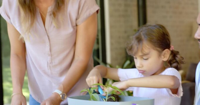 Family guiding child planting seedlings with blue trowel beside purple spray bottle on porch