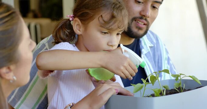 African family guiding child at porch table, child squeezing sprayer and watering planter seedlings