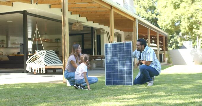 Family parents pointing toward roof and explaining solar panel install on lawn while child reaching