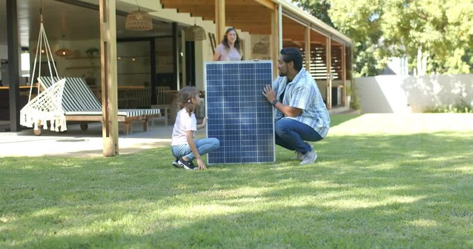 Diverse family steadying large solar panel needing support while placing upright on lawn near porch