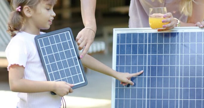 Mother pointing at solar cells, guiding child touching panel, showing wiring with juice on porch