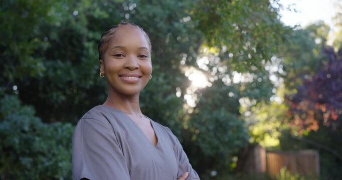 African American woman turning, smiling in garden under branches while camera shifting, in scrubs