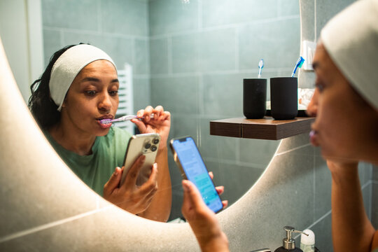 Woman brushing teeth while using smartphone in bathroom