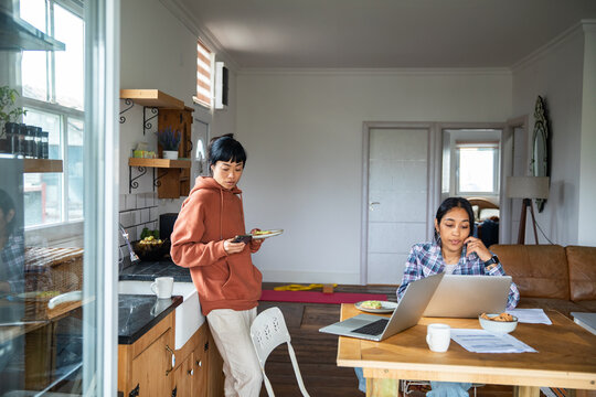 Two women working from home with laptops in kitchen