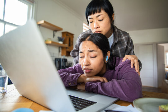 Concerned partner comforting stressed woman using laptop at home