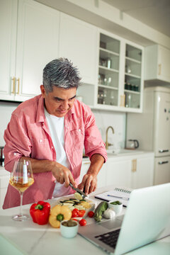 Middle-aged man cooking vegetables while following recipe in modern kitchen
