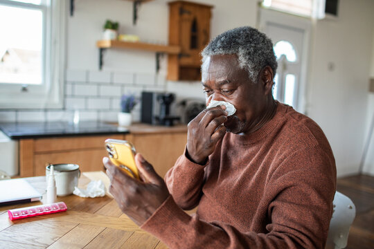 Senior man with tissue using smartphone at home kitchen