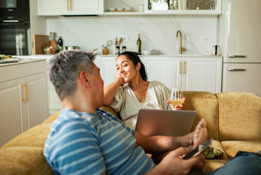 Couple relaxing on sofa with wine and laptop in modern kitchen