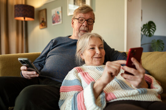 Senior couple using smartphones on sofa at home