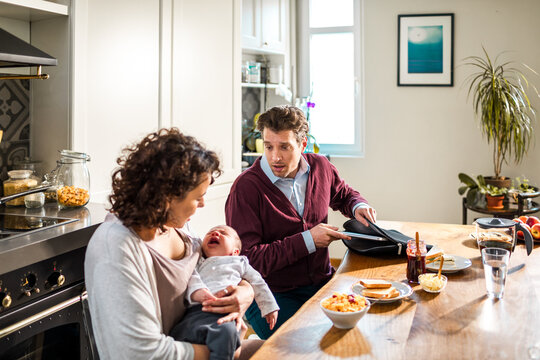 Parents comforting crying newborn at kitchen breakfast table