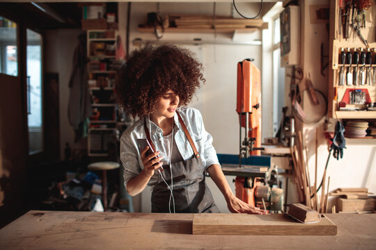 Woman woodworker sanding plank in carpentry workshop